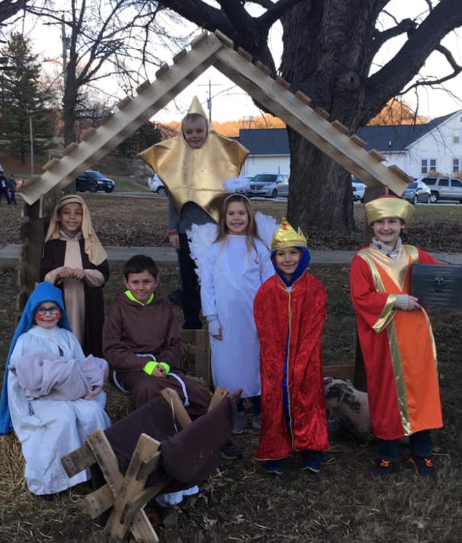 Children in nativity costumes posing under a wooden stable structure