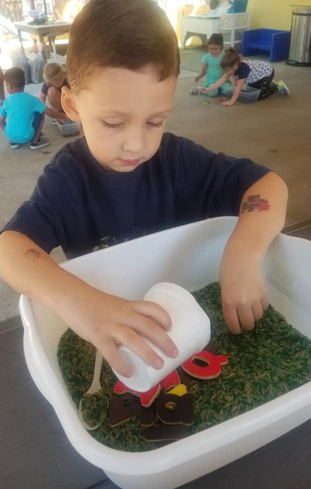 Child playing with green rice and letters in a bin