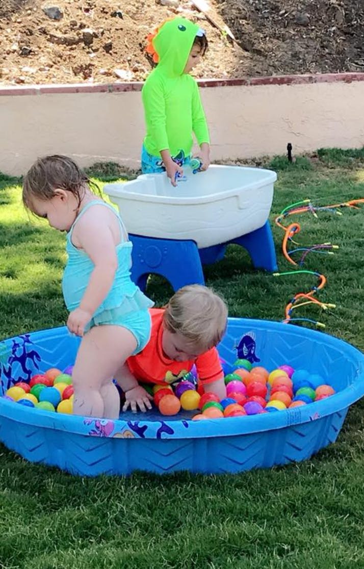 Three children playing with water and balls in a yard