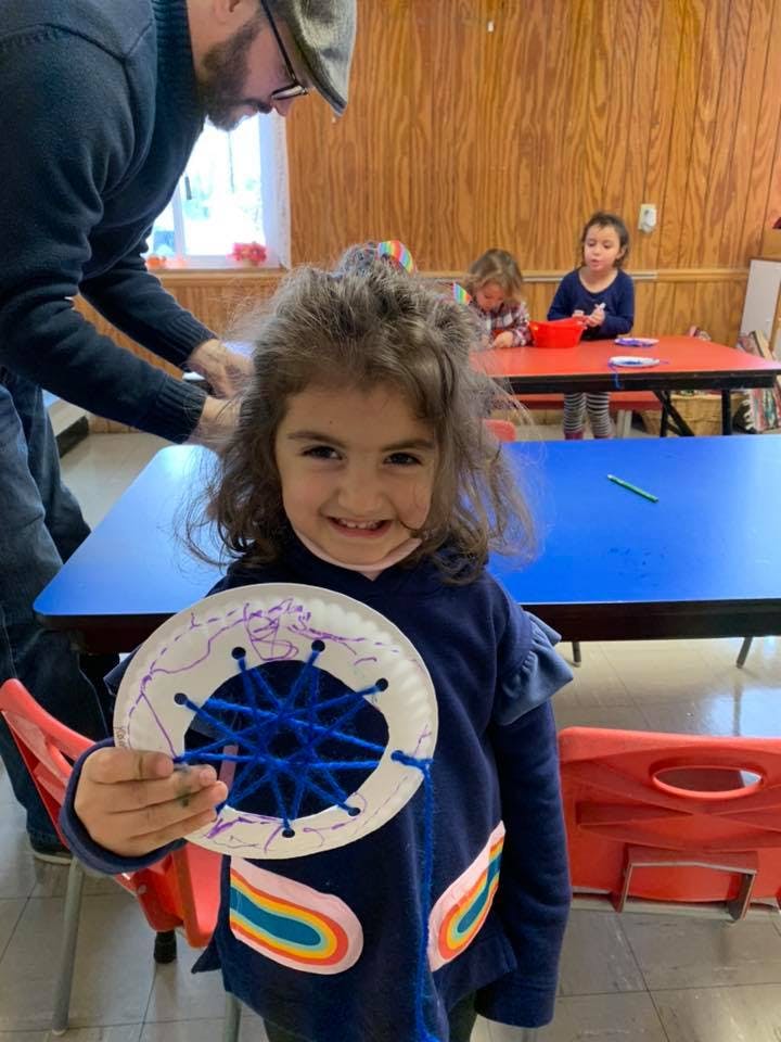 Child holding a paper plate craft with blue yarn