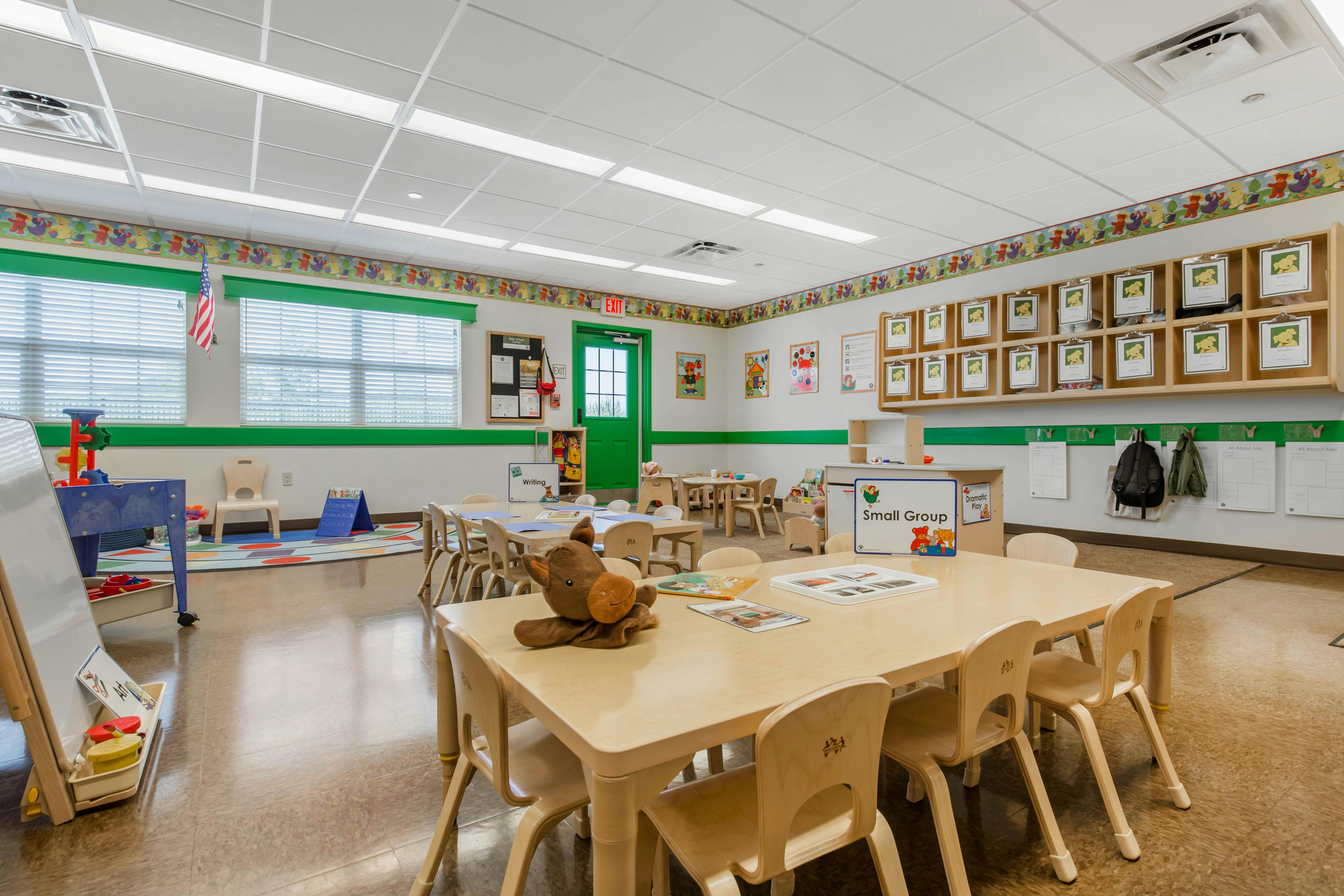 Classroom with small tables and chairs, a play rug, and activity centers