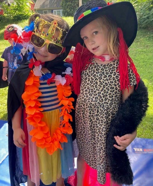 Two children in costumes, one with a crown and sunglasses, the other in a hat