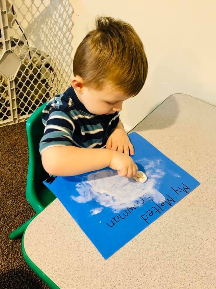 Child creating art on a blue paper with white paint