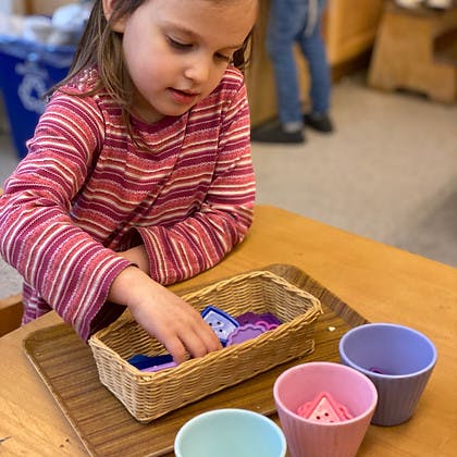Child reaching into a basket of small shapes in a classroom