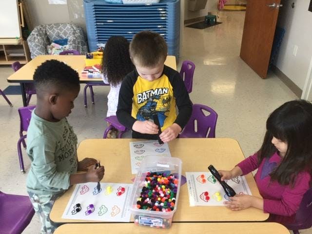 Three children at a table working on crafts with pom-poms