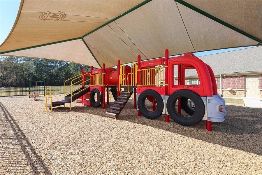 Red fire truck shaped playground equipment under a shade canopy