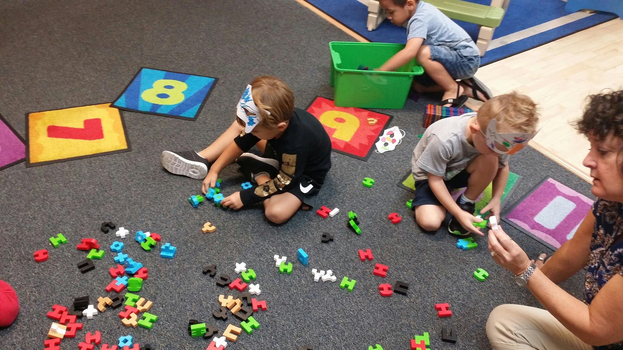 Adult and children playing with colorful letter and number shapes on a floor