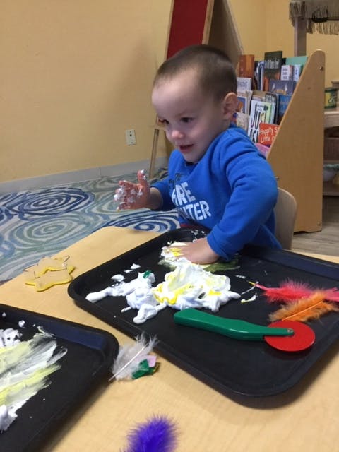 Child playing with white and yellow paint on a black tray