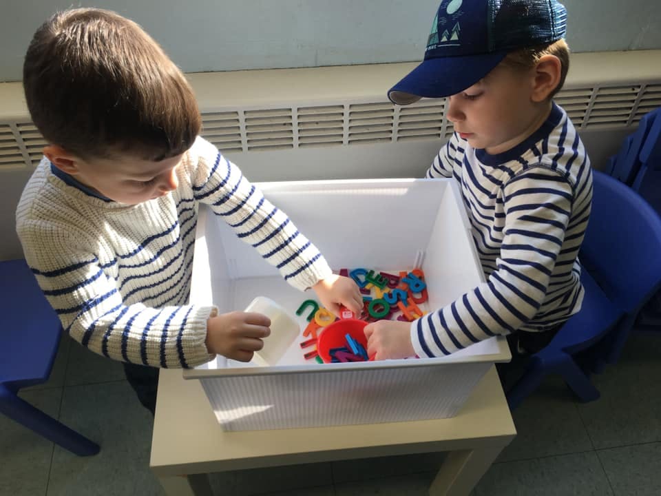 Two children playing with colorful letter toys in a white bin
