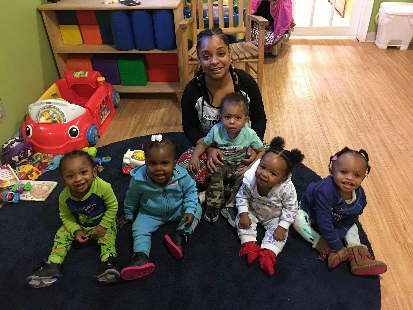 Adult and five children sitting on a rug in a room with toys