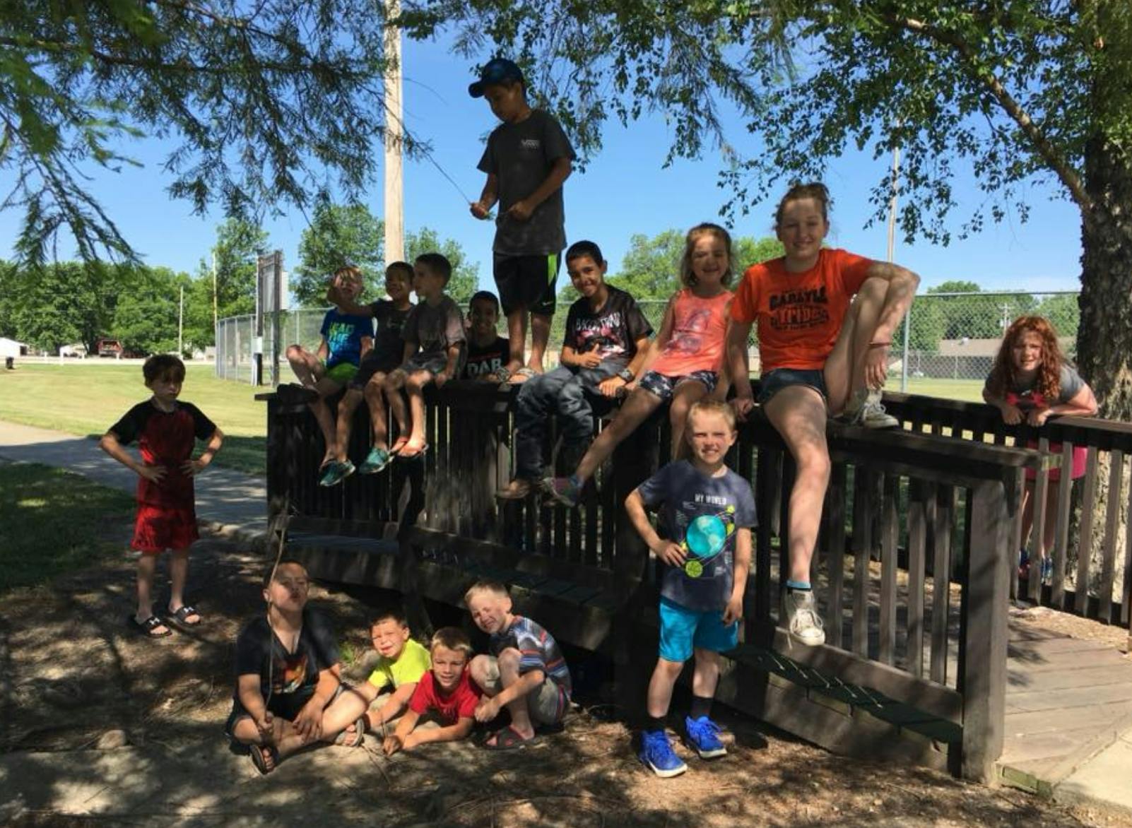 Group of children and teens posing on and around a wooden fence outdoors