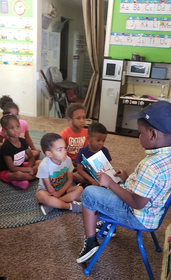 Child reading a book to other children sitting on the floor