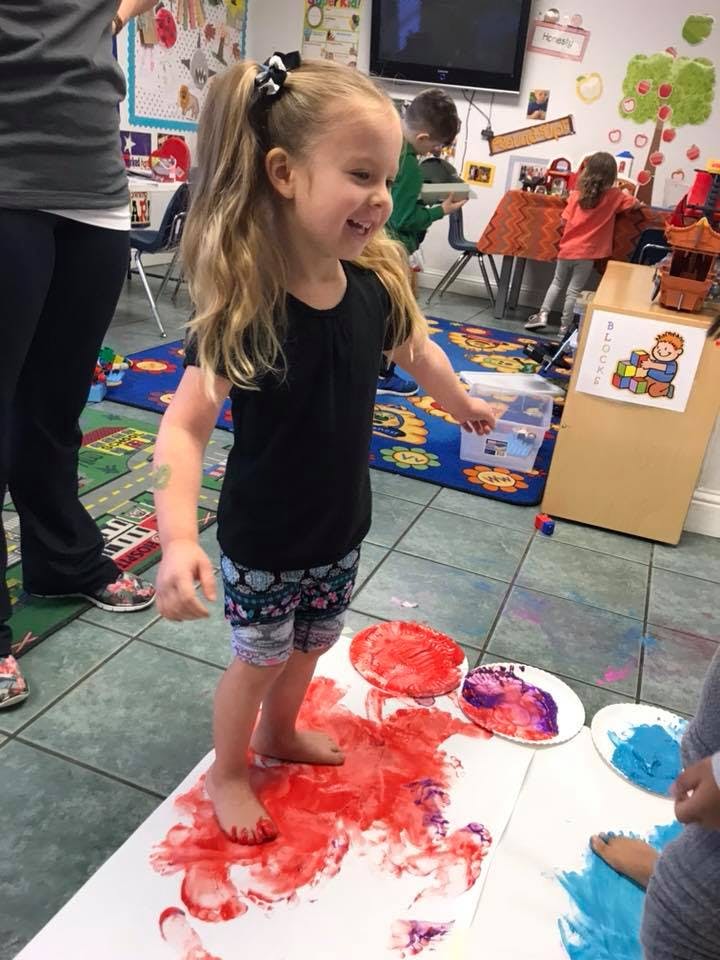 Child standing barefoot in red paint on paper