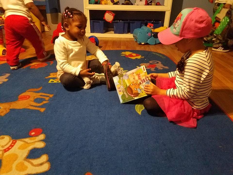 Two children sitting on a rug looking at a book