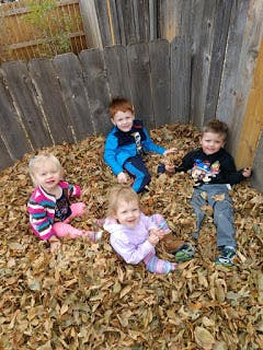 Four children sitting in a pile of autumn leaves