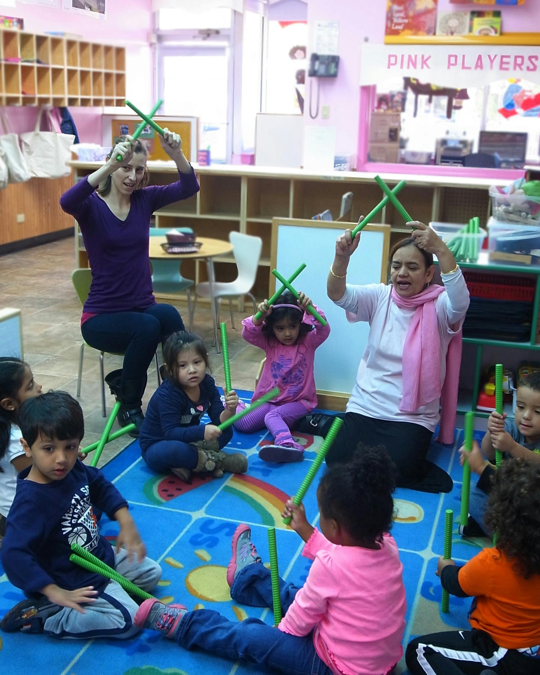 Adults and children in a classroom holding green sticks