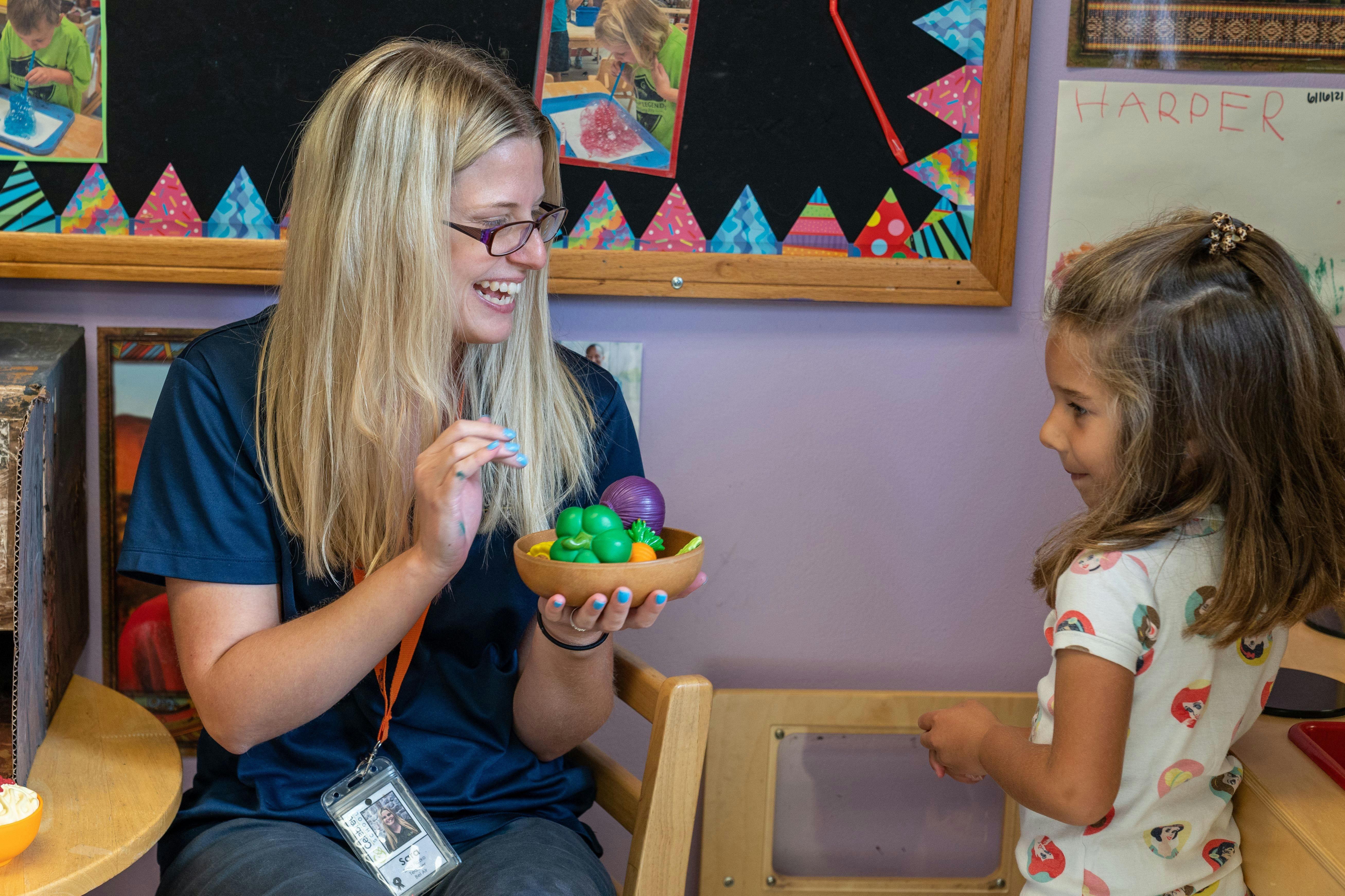 Adult and child interacting with small colorful objects in a classroom