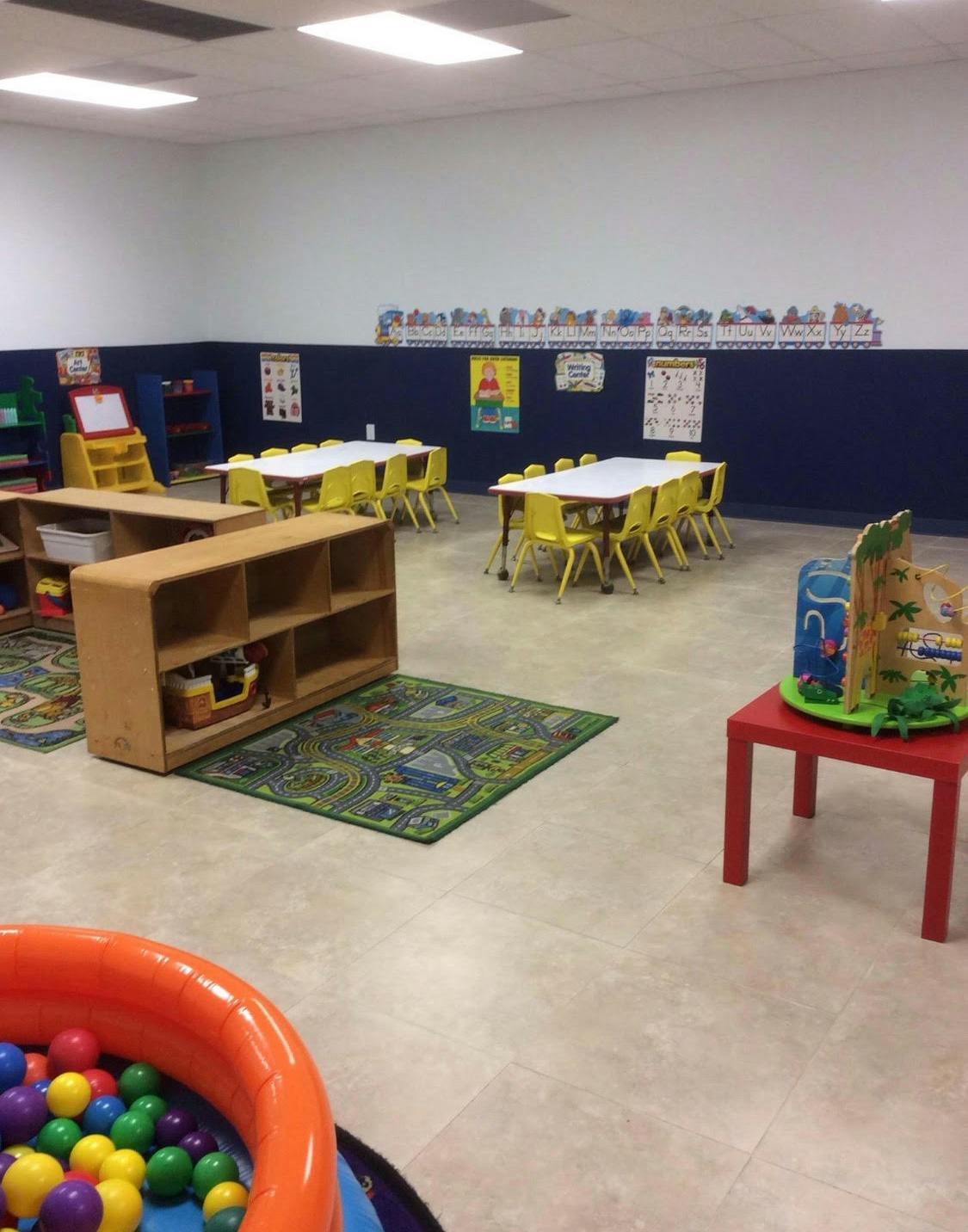Classroom with small tables and chairs, shelves, and a ball pit