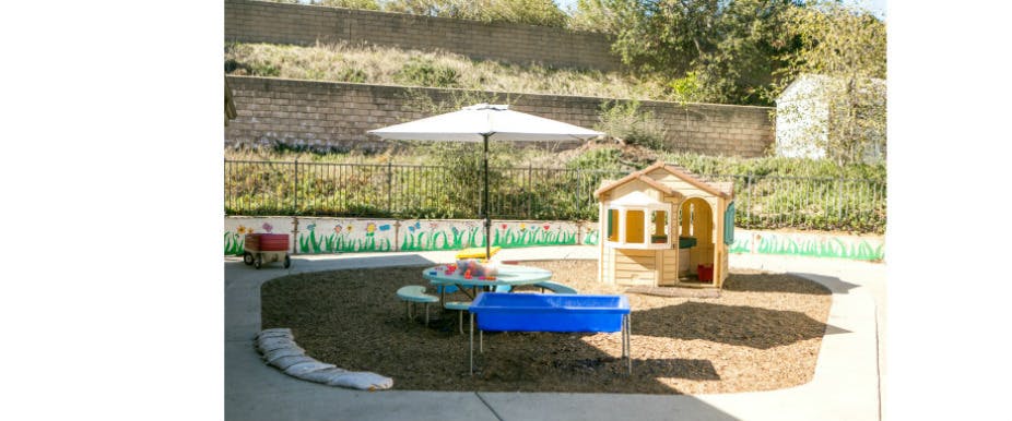 Play area with a small playhouse, umbrella, and sand table