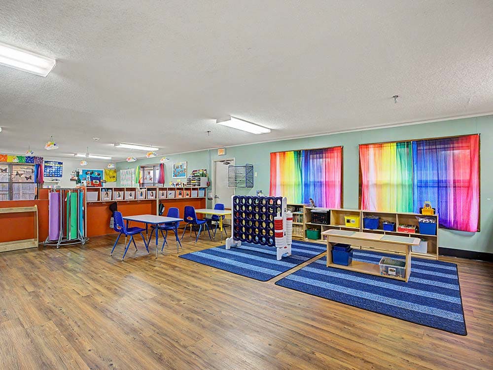 Empty classroom with small tables and chairs, colorful curtains, and learning materials