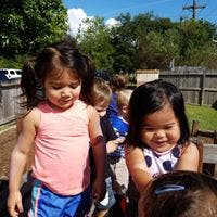 Two children standing outdoors with other children in the background