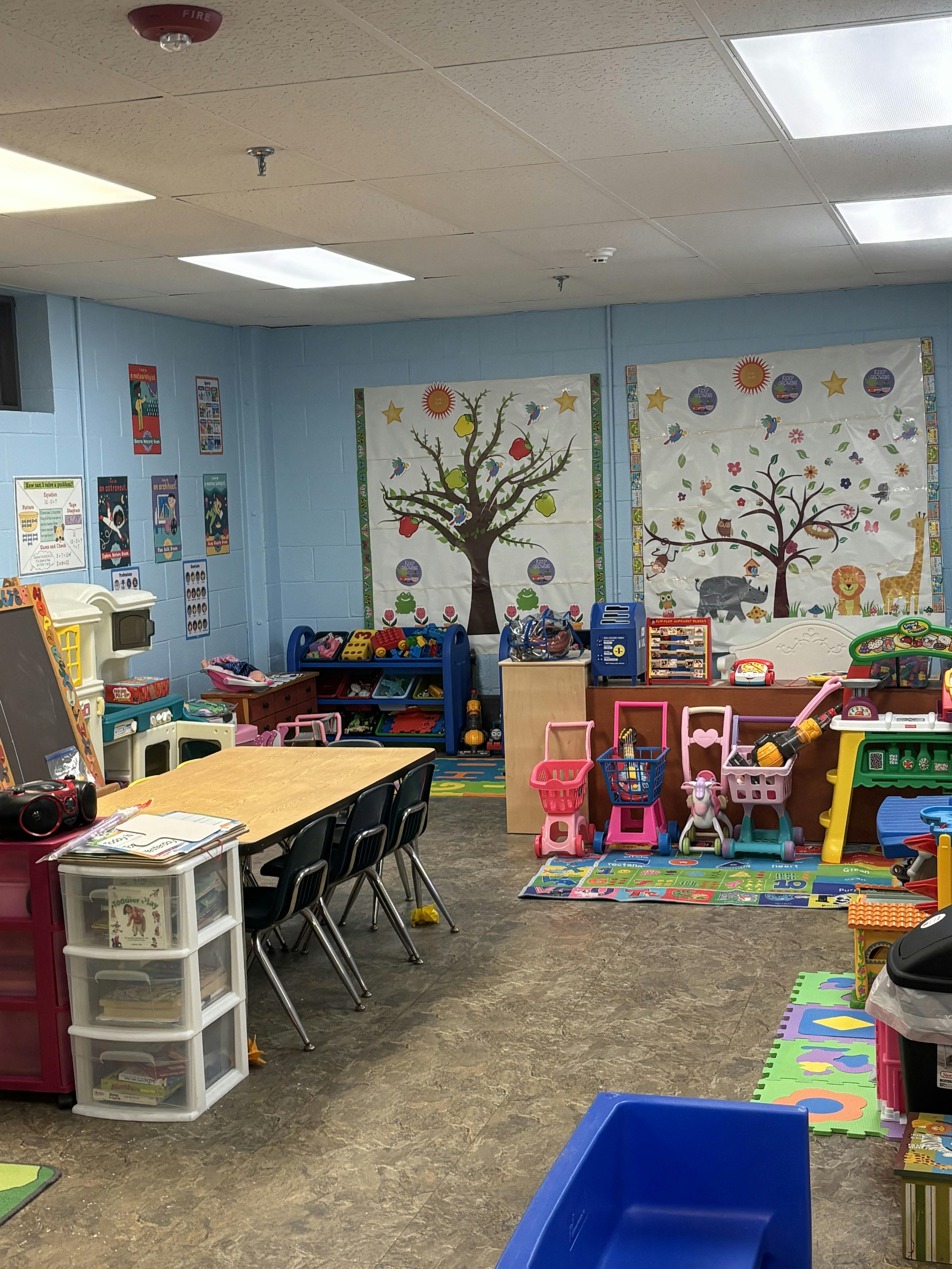 Classroom with tables, chairs, colorful playmats, toys, and educational posters