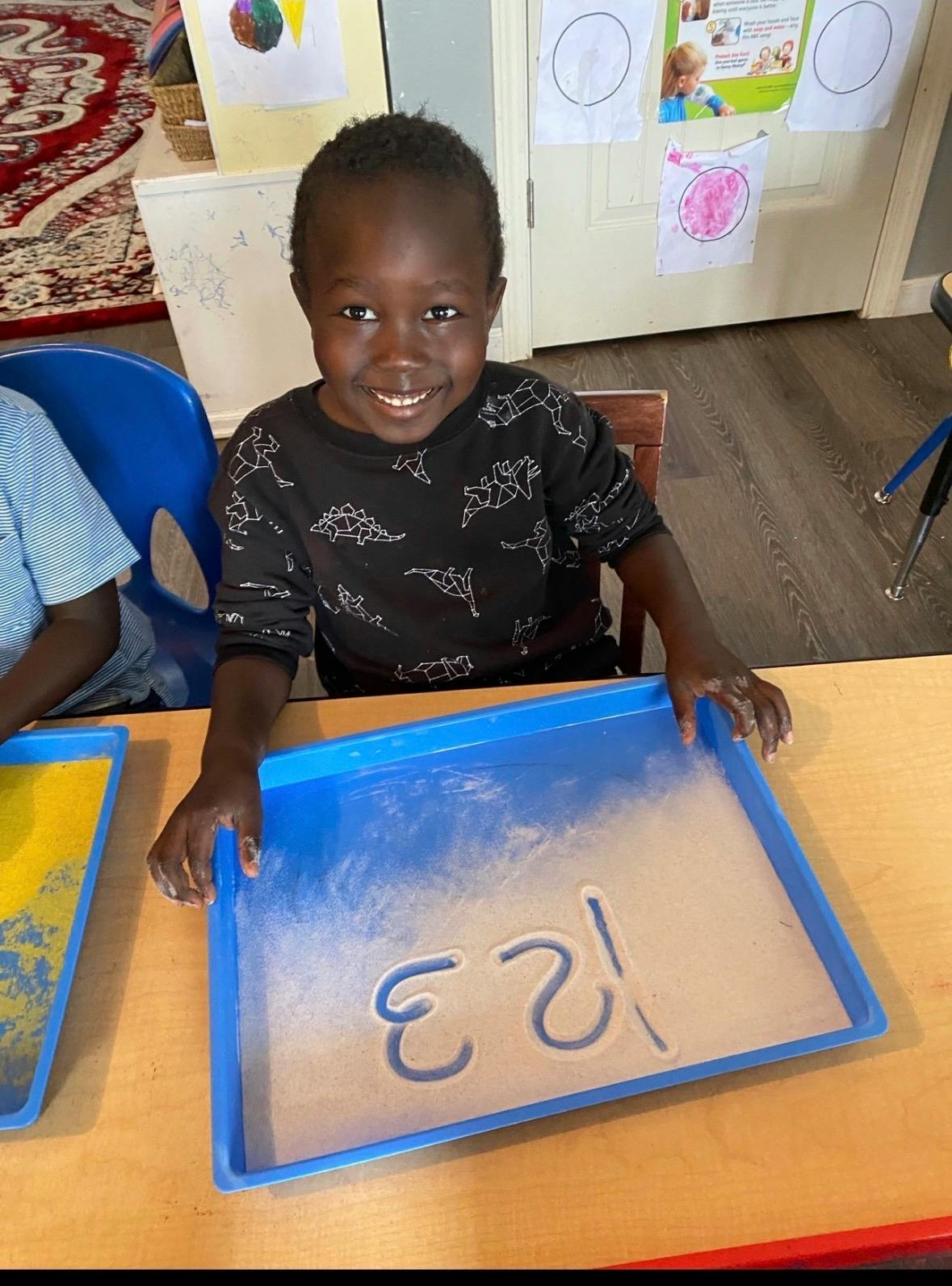 Child drawing numbers in a sand tray in a classroom