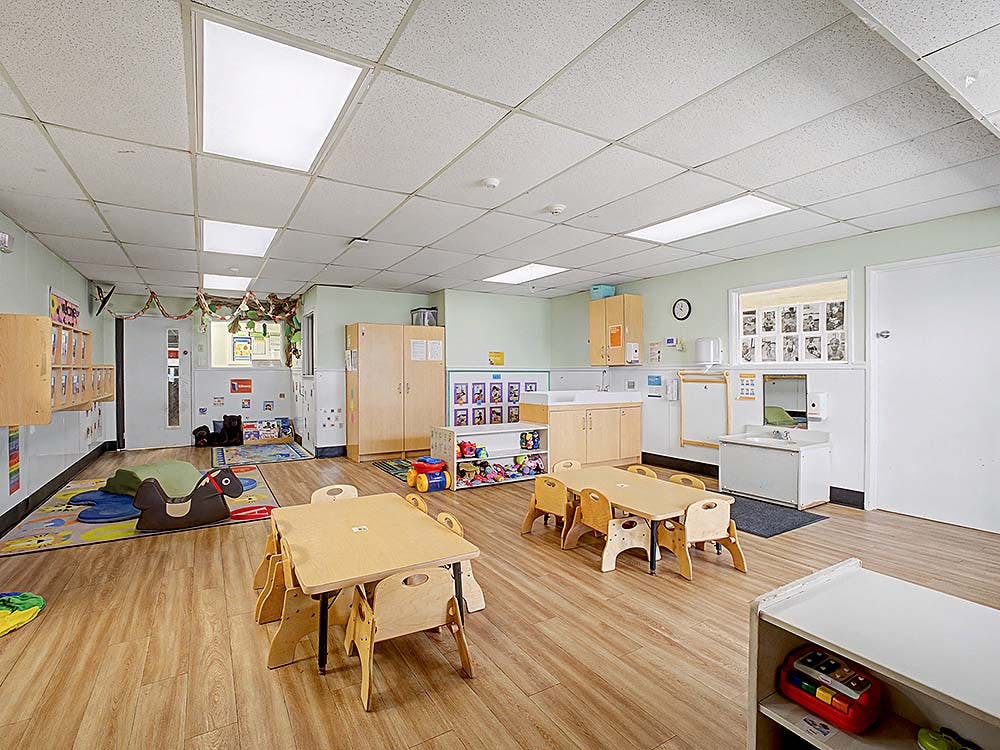 Classroom with small tables and chairs, play mats, and a sink area