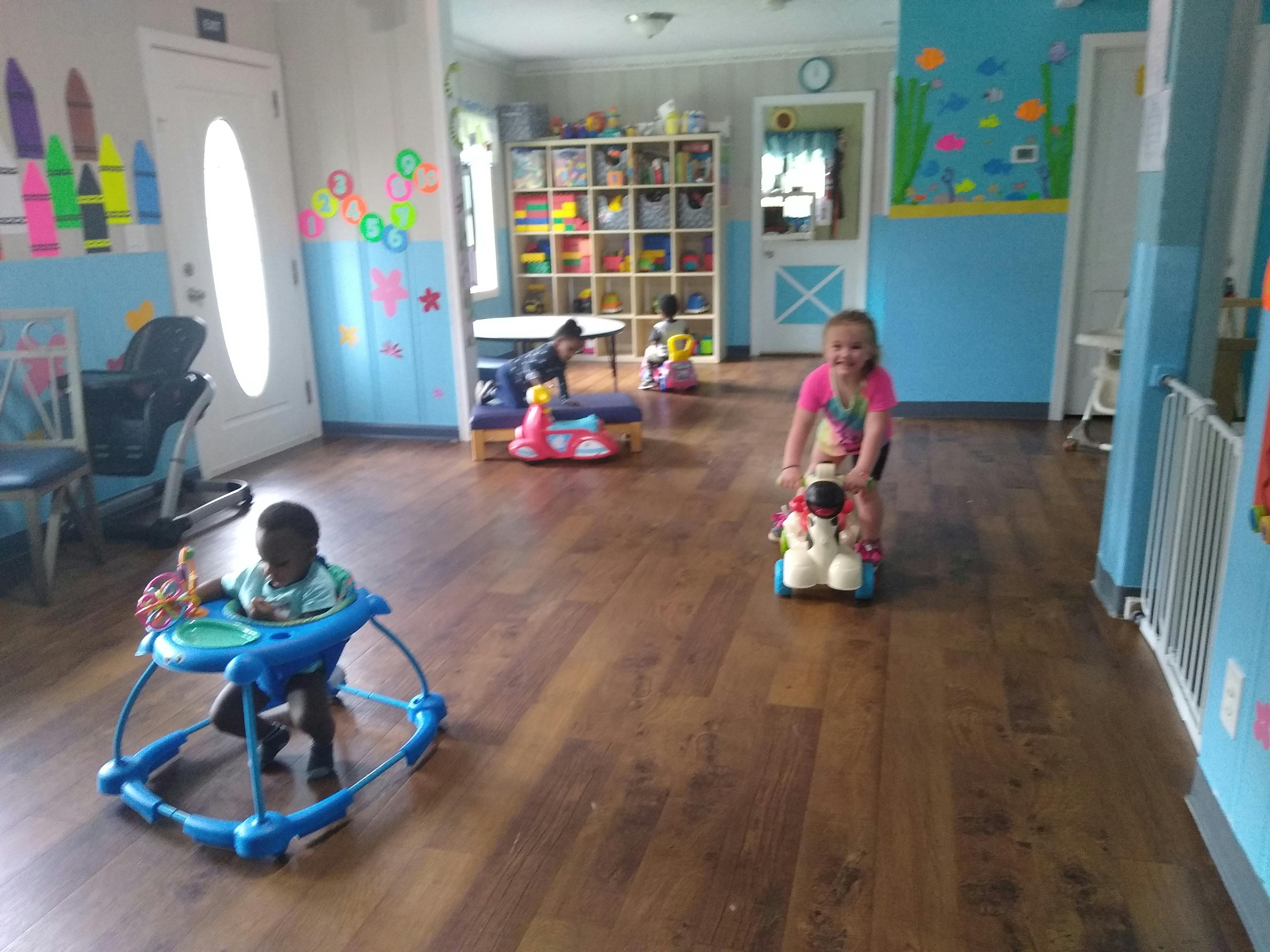 Child in a walker and child on a ride-on toy in a playroom
