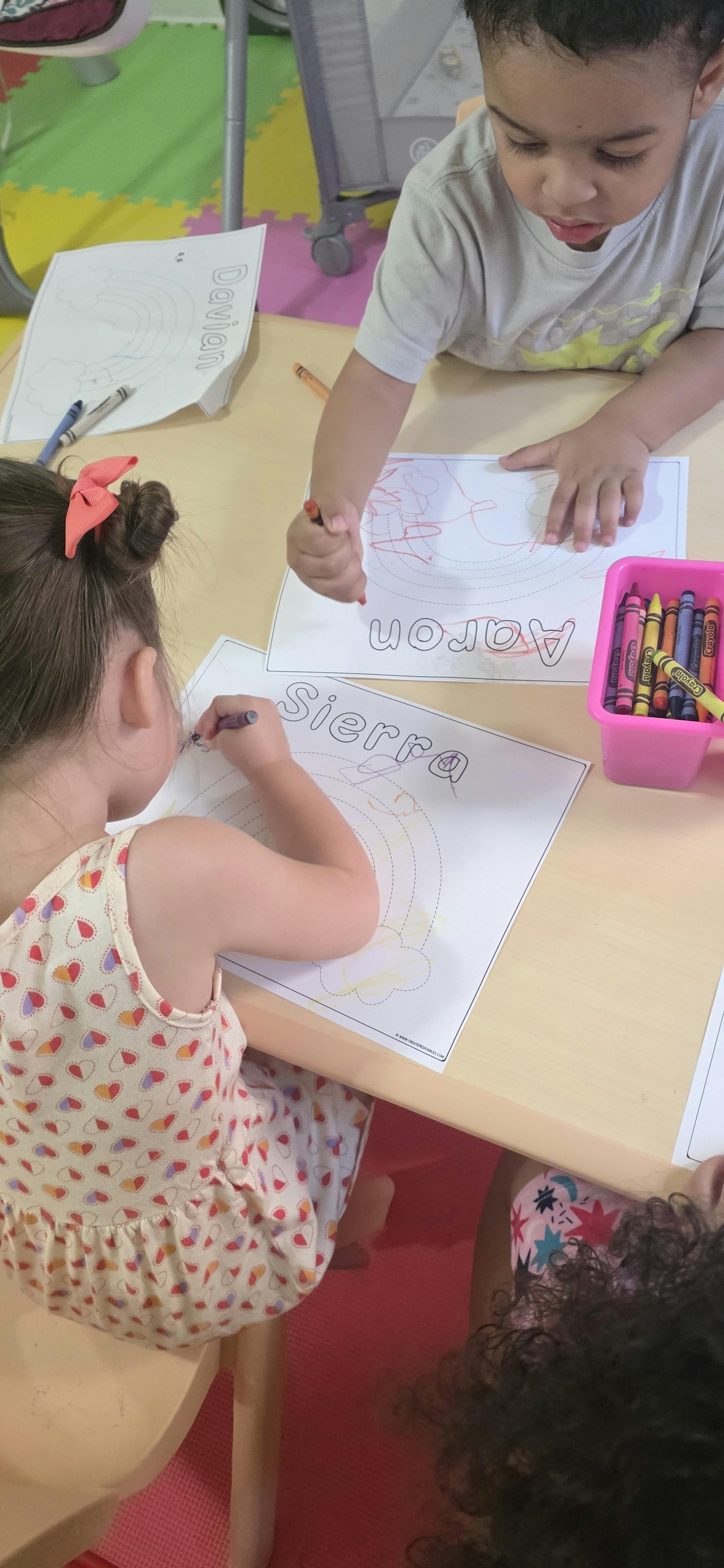 Children coloring names on paper at a table