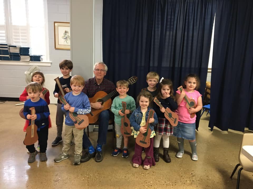 Adult and children holding guitars and ukuleles
