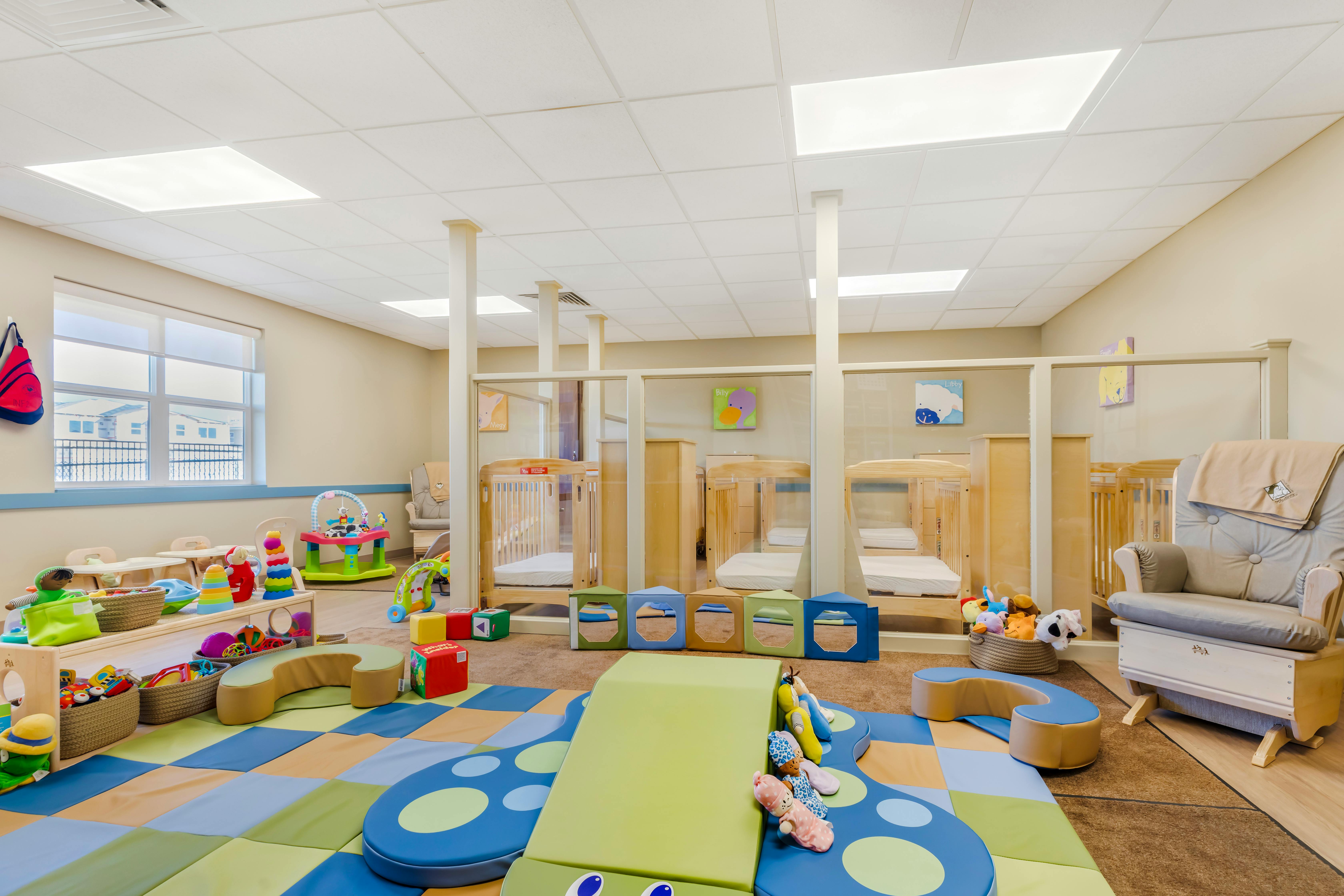 Daycare room with play mats, toys, and cribs