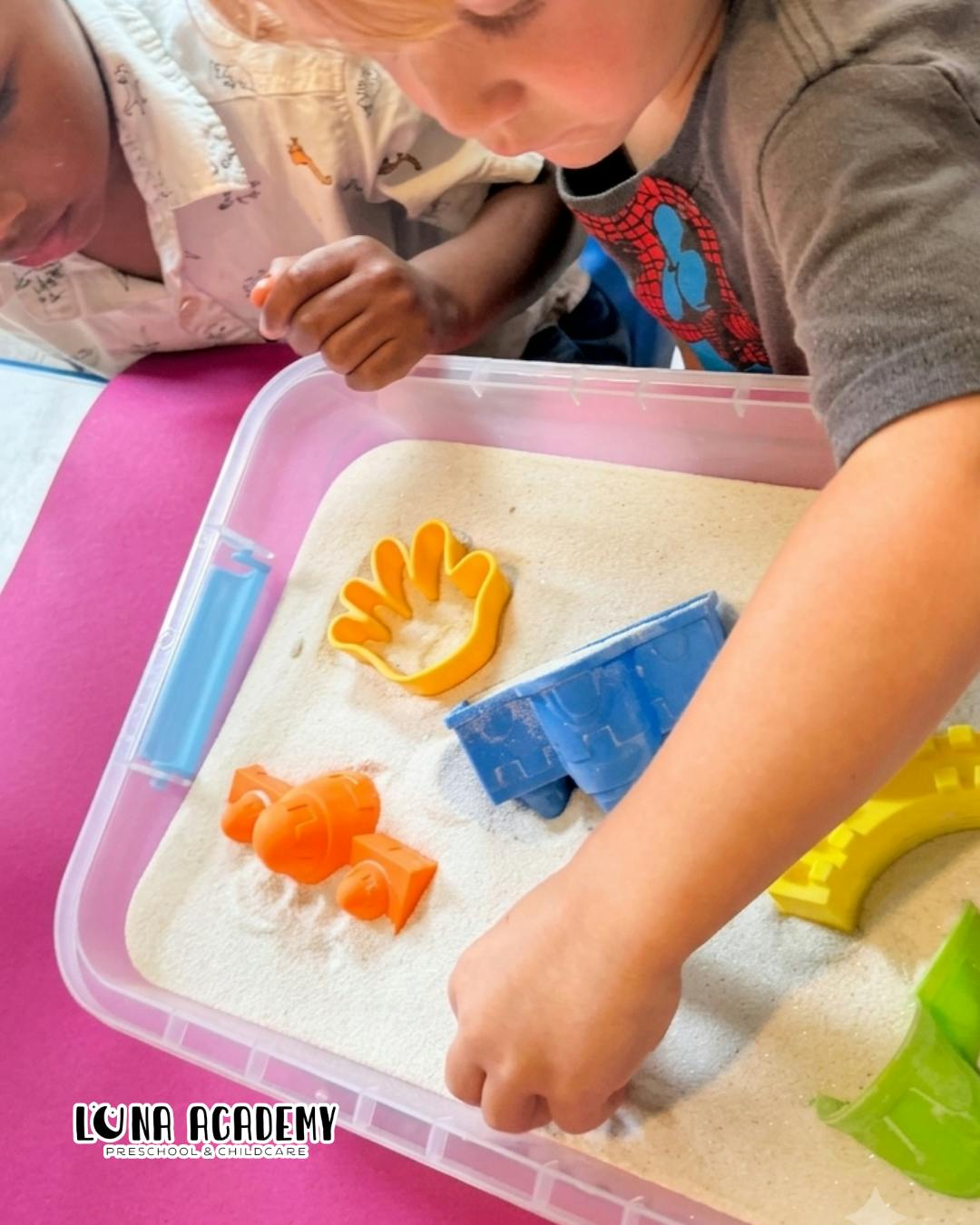Children playing with sand and plastic molds in a sensory bin