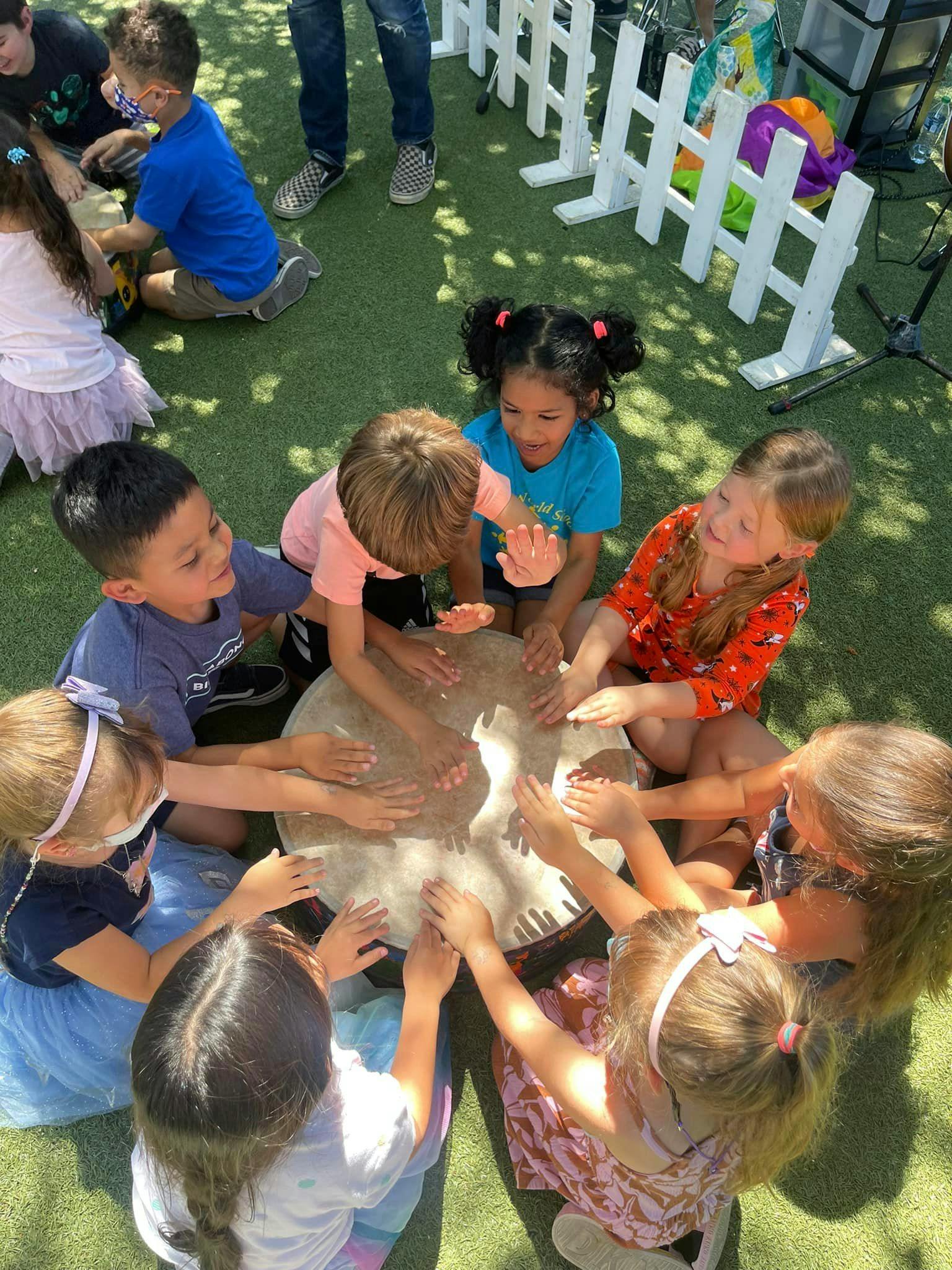 Children gathered around a drum, playing it with their hands
