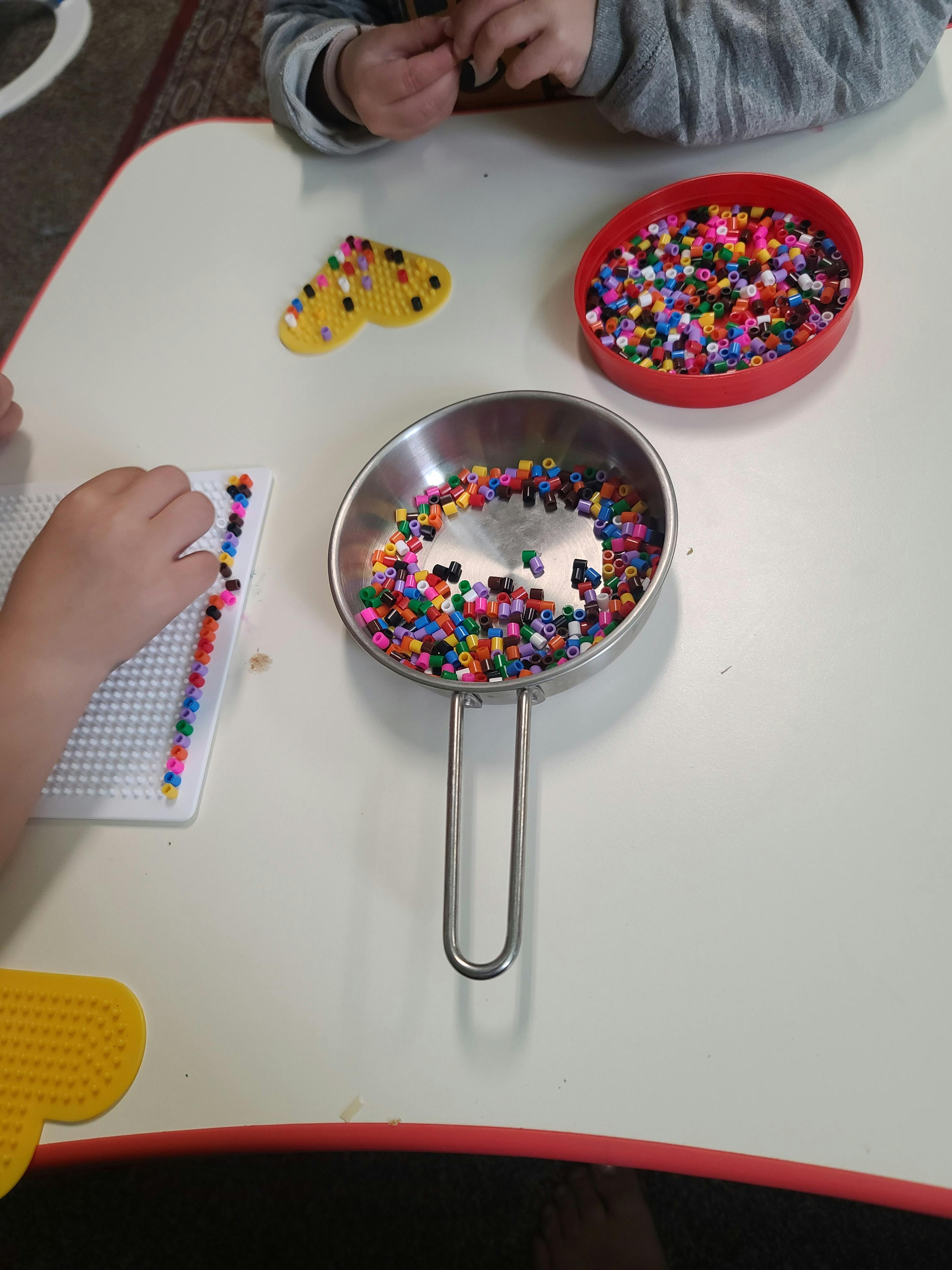 Person's hands working with colorful beads on a white pegboard