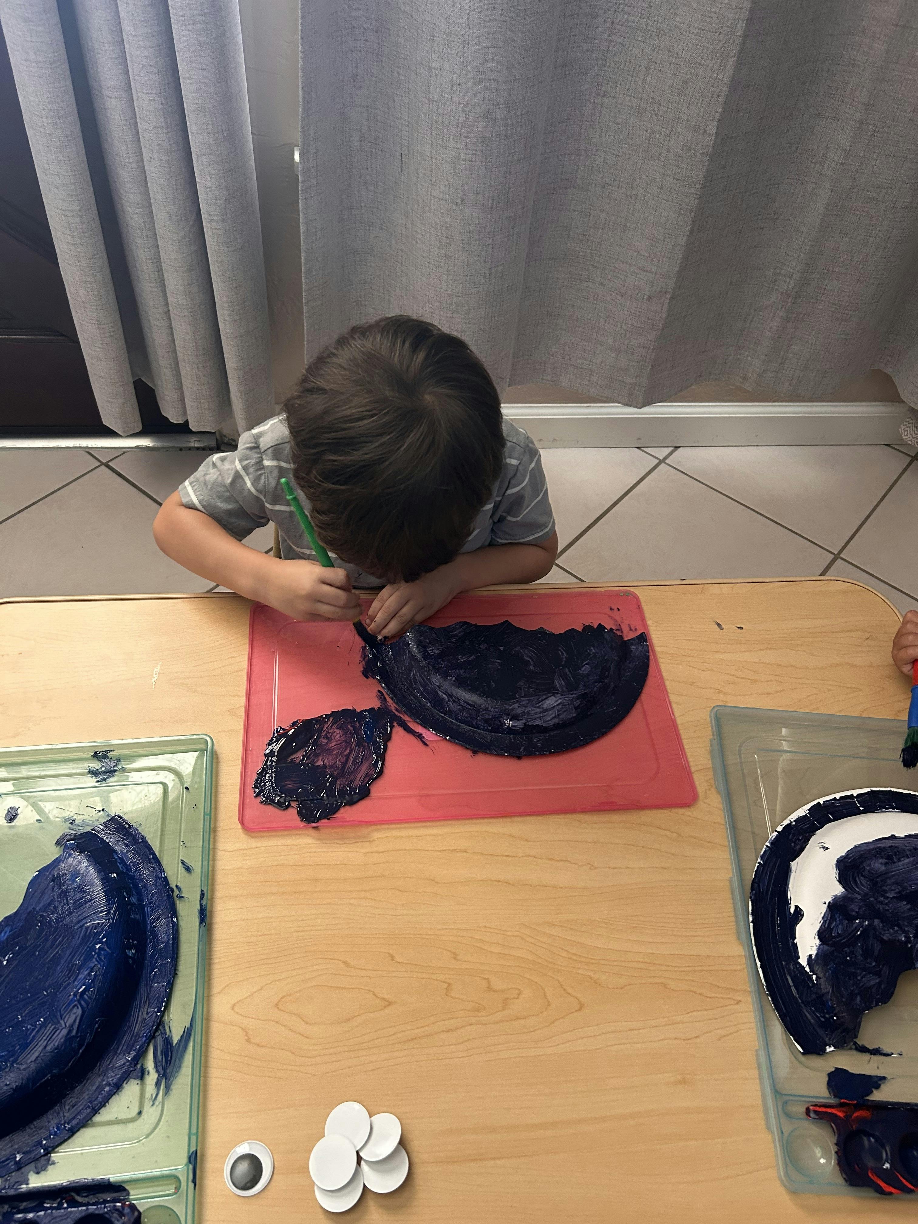 Child painting on a paper plate at a table