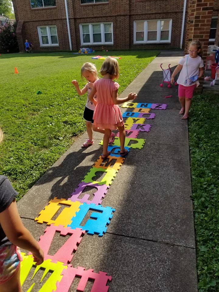 Children playing on colorful alphabet mats on a sidewalk