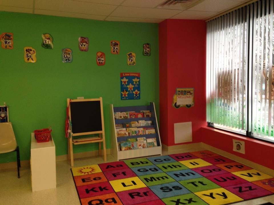 Classroom with green and red walls, an easel, a bookshelf, and an alphabet rug