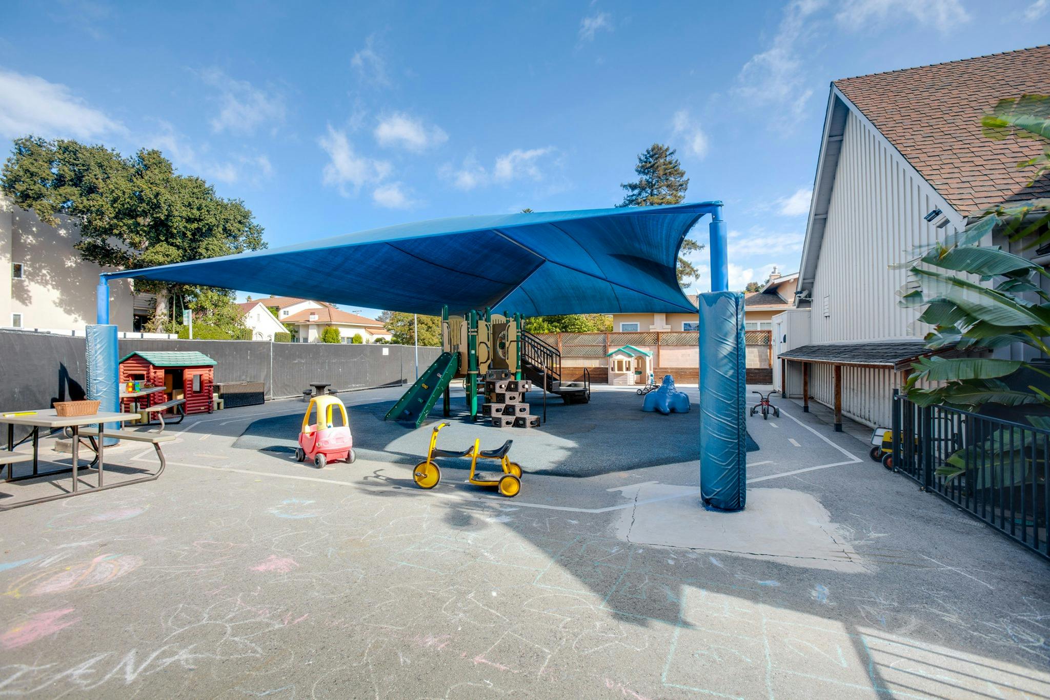 Outdoor playground with a blue shade structure, play equipment, and toys