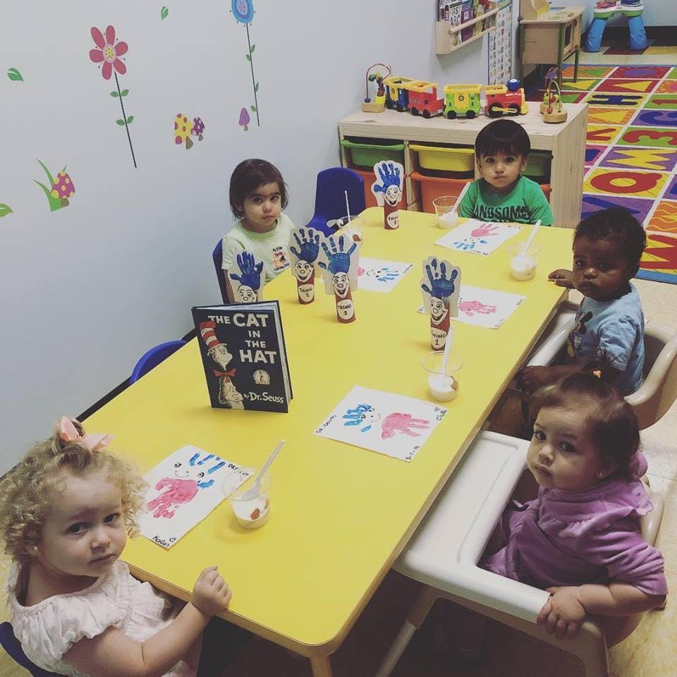 Four children sitting at a yellow table with craft supplies and a book