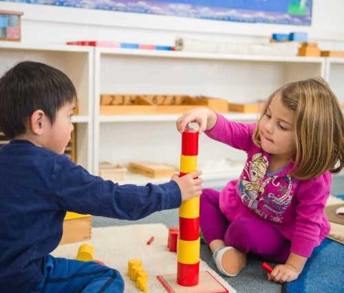 Two children building a tower with red and yellow blocks
