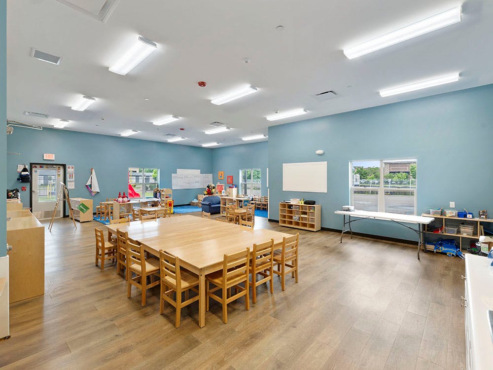 Classroom with light blue walls, wooden floors, and children-sized tables and chairs
