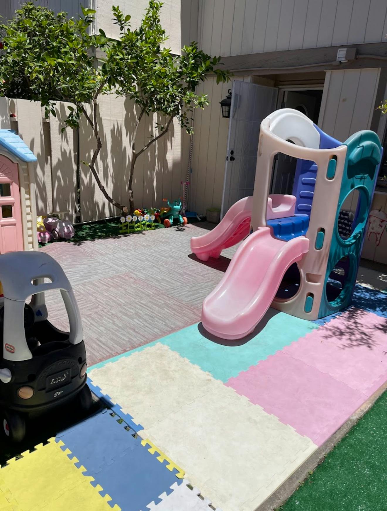 Outdoor play area with a toy car, playhouse, and slide on colorful mats