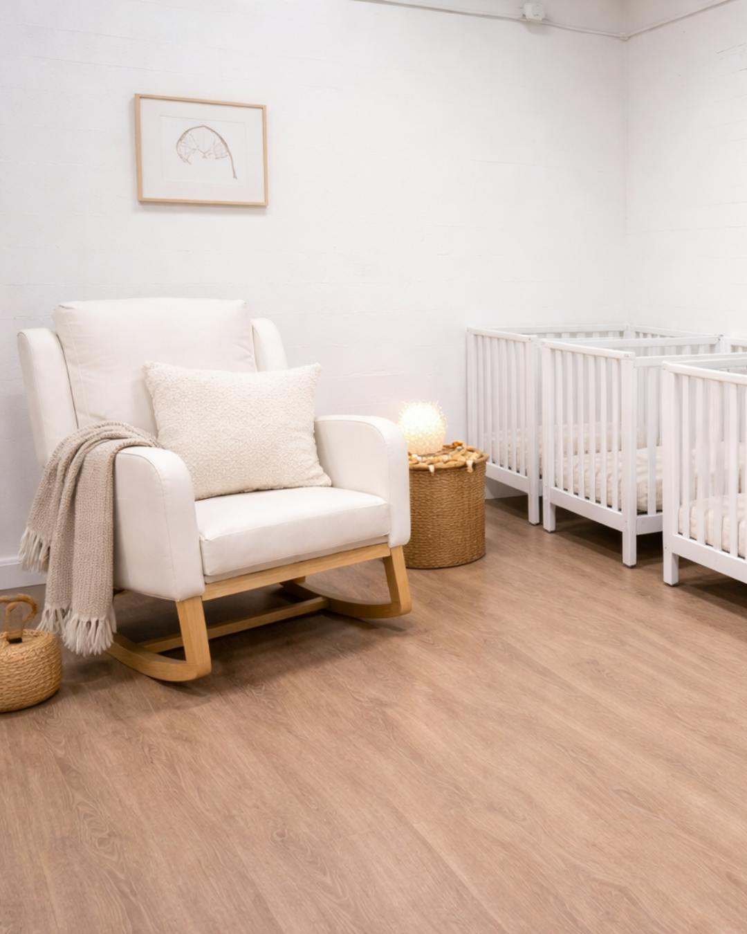 White rocking chair with blanket and pillow next to cribs in a room