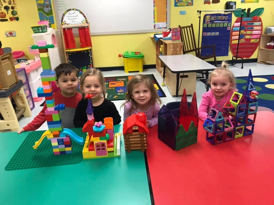 Three children and a teen with block creations in a classroom