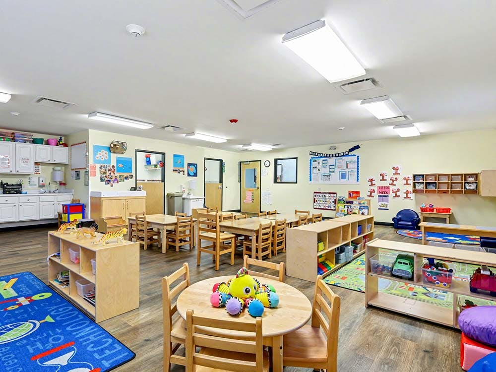 Classroom with small tables and chairs, shelves with toys, and posters on walls