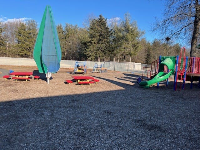 Playground area with red picnic tables, a covered umbrella, and a green slide