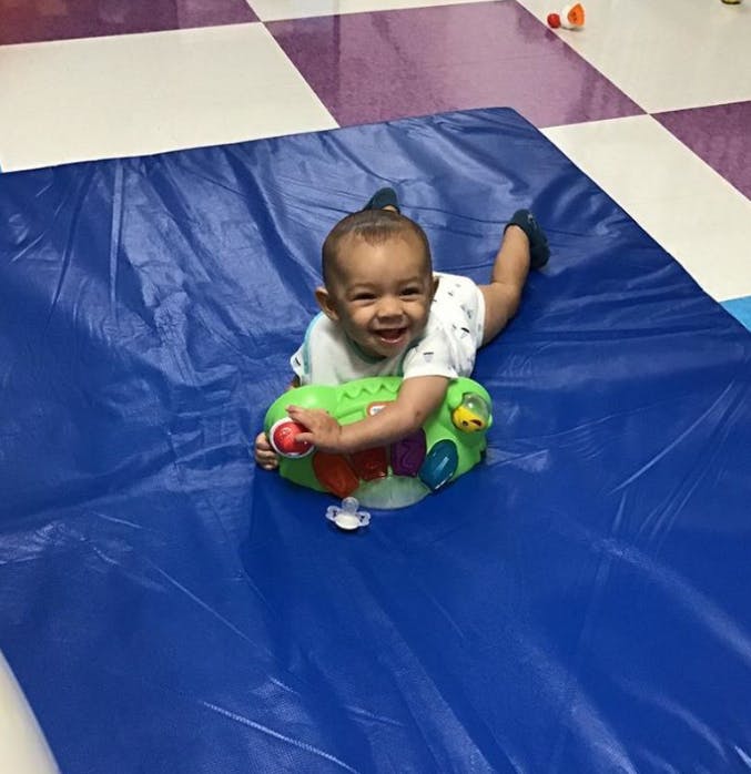 Child on stomach on blue mat with a green toy