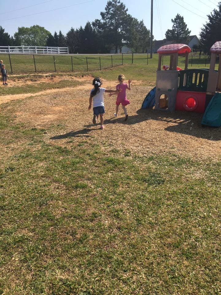 Two children running on a playground near a play structure