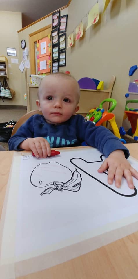 Child sitting at a table with a coloring page and a red crayon